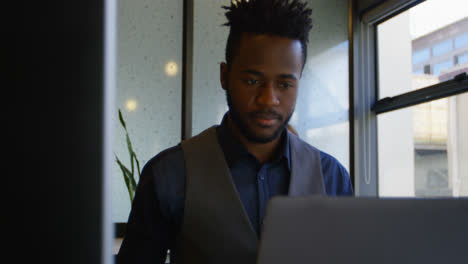 Front-view-of-young-black-businessman-working-on-laptop-at-desk-in-a-modern-office-4k