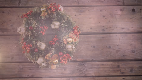 Digital-composition-of-spots-of-light-against-christmas-wreath-decoration-on-wooden-surface