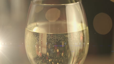 Digital-composition-of-golden-spots-of-light-against-wine-glass-on-wooden-surface