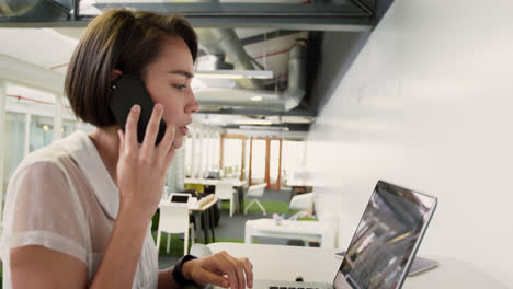 Mujer-De-Negocios-Hablando-Por-Teléfono-Móvil-Mientras-Usa-Una-Computadora-Portátil-En-La-Oficina-Moderna-4k