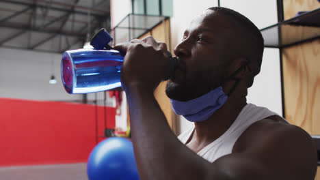 Afroamerikanischer-Mann-Mit-Heruntergelassener-Gesichtsmaske-Trinkt-Im-Fitnessstudio