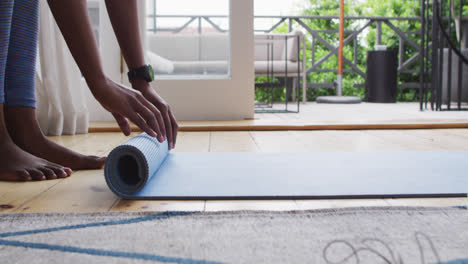 Mid-section-of-african-american-woman-rolling-yoga-mat-at-home