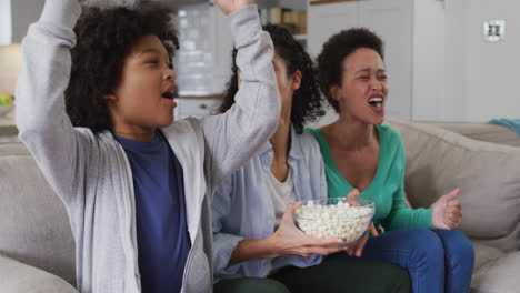 Mixed-race-lesbian-couple-and-daughter-watching-tv-eating-popcorn-high-fiving