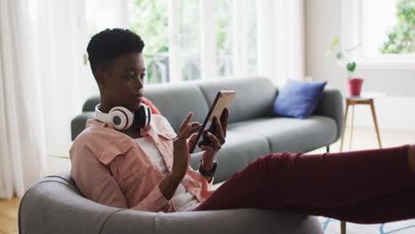 Afroamerikanische-Frau,-Die-Ein-Digitales-Tablet-Benutzt,-Während-Sie-Zu-Hause-Auf-Der-Couch-Sitzt