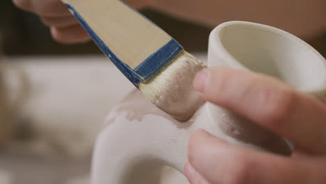 Close-up-view-of-female-potter-using-glaze-brush-to-paint-on-pot-at-pottery-studio