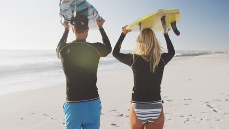 Caucasian-couple-holding-surfboards-on-the-beach