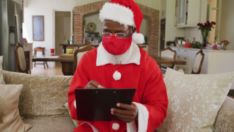Senior-african-american-man-at-christmas-time-wearing-red-face-mask-and-santa-costume
