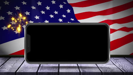 Digital-animation-of-smartphone-on-wooden-surface-against-fireworks-exploding-against-waving-us-flag