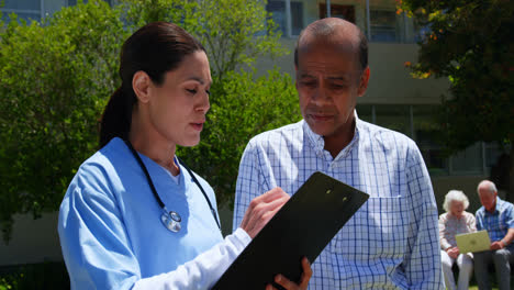 Front-view-of-active-Asian-senior-man-and-female-doctor-discussing-over-medical-report-in-the-garden