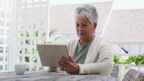 Senior-mixed-race-woman-having-coffee-using-tablet-in-garden