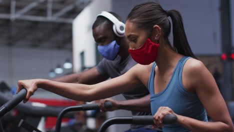 Mixed-race-woman-wearing-face-mask-exercising-at-gym