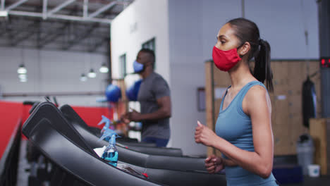 Fit-caucasian-woman-wearing-face-mask-running-on-treadmill-in-the-gym