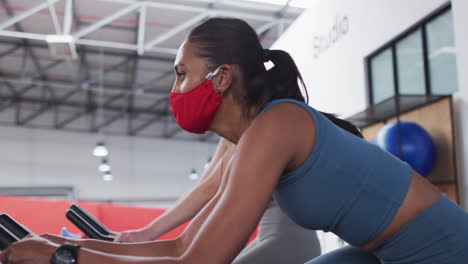 Diverse-women-wearing-face-masks-exercising-at-gym