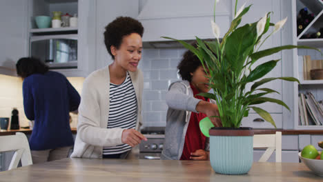 Mixed-race-lesbian-couple-and-daughter-watering-plants-in-kitchen