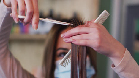Female-hairdresser-wearing-face-mask-cutting-hair-of-female-customer-at-hair-salon