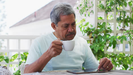 Älterer-Mann-Mit-Gemischter-Abstammung-Trinkt-Kaffee-Mit-Tablet-Im-Garten