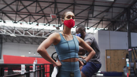 Mixed-race-female-fitness-trainer-wearing-face-mask-at-gym