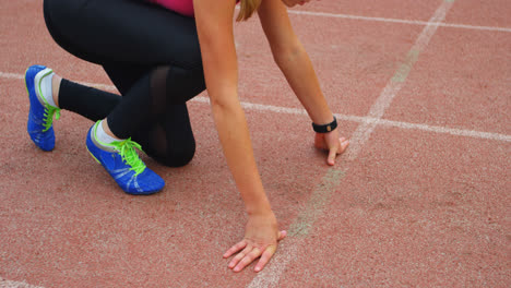 Side-view-of-Caucasian-female-athlete-taking-starting-position-on-a-running-track-at-sports-venue-4k