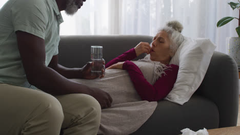 African-american-man-giving-medication-to-his-sick-wife-in-the-living-room-at-home