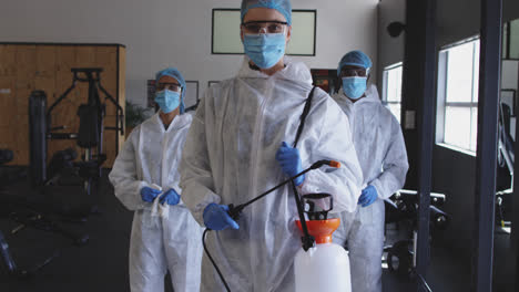 Team-of-health-workers-wearing-protective-clothes-holding-disinfectant-sprayer-in-the-gym