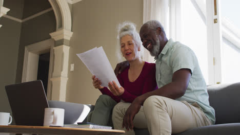 Mixed-race-senior-couple-discussing-finances-together-in-the-living-room-at-home