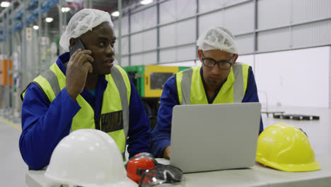 Warehouse-workers-using-laptop-in-factory