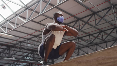 Afroamerikanischer-Mann-Springt-Mit-Gesichtsmaske-Im-Fitnessstudio-Auf-Eine-Kiste