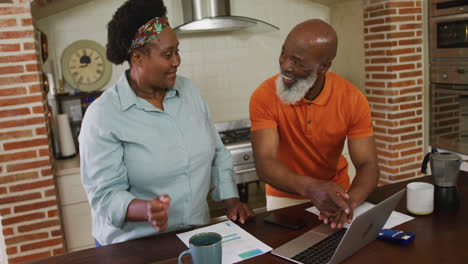 Feliz-Pareja-De-Ancianos-Afroamericanos-Usando-Una-Computadora-Portátil-En-La-Cocina-De-Casa