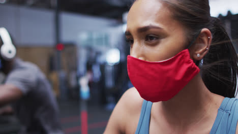 Mixed-race-woman-wearing-face-mask-exercising-at-gym