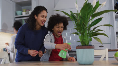 Mixed-race-lesbian-couple-and-daughter-watering-plants-in-kitchen