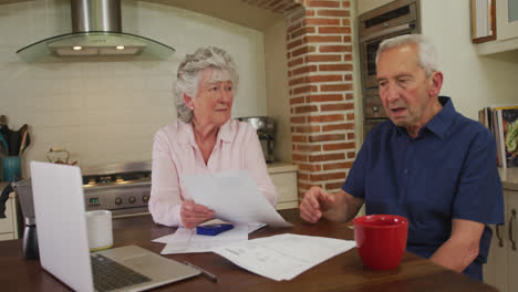 Senior-caucasian-couple-sitting-in-kitchen-checking-paperwork