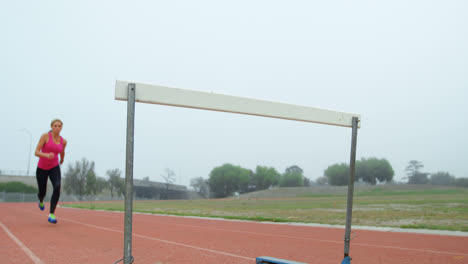 Niedriger-Winkel-Einer-Kaukasischen-Sportlerin,-Die-Auf-Der-Rennstrecke-4k-über-Eine-Hürde-Springt