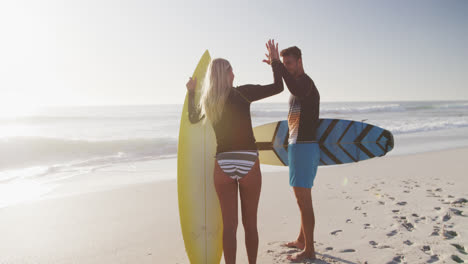 Caucasian-couple-holding-surfboards-on-the-beach