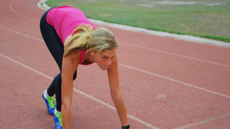 Front-view-of-Caucasian-female-athlete-taking-starting-position-and-running-on-a-track-at-sports-ven