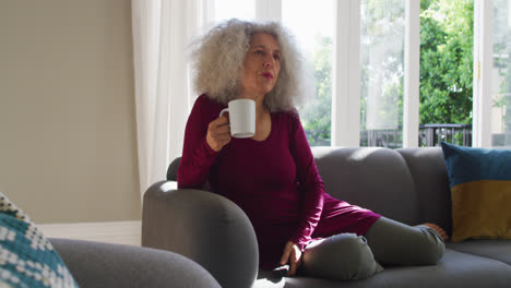 Senior-caucasian-woman-drinking-coffee-while-watching-tv-at-home