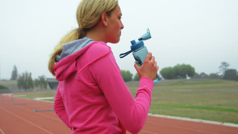 Side-view-of-Caucasian-female-athlete-drinking-water-on-race-track-4k