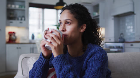 Mixed-race-woman-sitting-on-couch-and-drinking-coffee