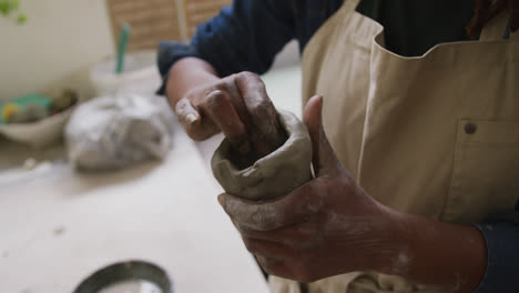 Mid-section-of-female-potter-wearing-apron-working-on-clay-to-create-pot-at-pottery-studio