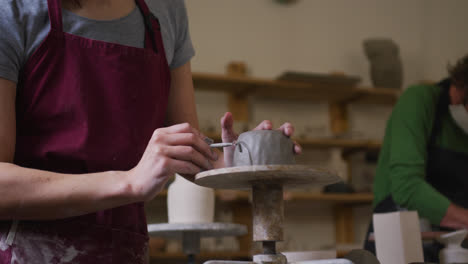 Mid-section-of-female-potter-wearing-apron-using-ribbon-tool-to-create-design-on-pot-at-pottery-stud