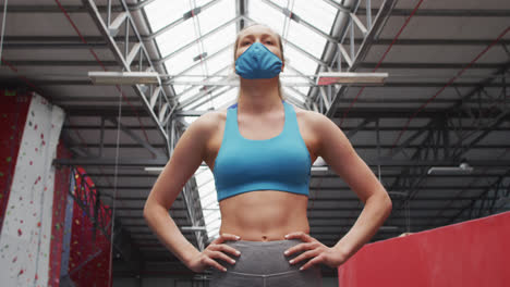 Fit-caucasian-woman-wearing-face-mask-standing-with-hands-on-her-hips-in-the-gym