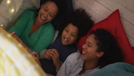 Mixed-race-lesbian-couple-and-daughter-using-smartphone-lying-in-bedroom-camp