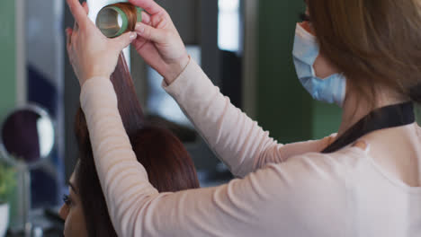 Female-hairdresser-wearing-face-mask-putting-rollers-on-hair-of-female-customer-at-hair-salon