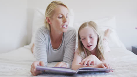 Front-view-of-Caucasian-woman-reading-a-story-to-her-daughter-on-bed