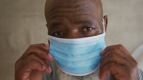 Close-up-of-portrait-of-african-american-senior-man-wearing-face-mask-at-home