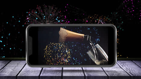 Animation-of-champagne-bottle-and-glass-on-smartphone-screen-and-fireworks-in-the-background