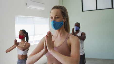 Diverse-fit-people-wearing-face-masks-performing-yoga-in-yoga-studio