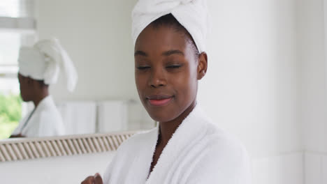 Portrait-of-african-american-woman-in-bathrobe-smiling-in-the-bathroom-at-home