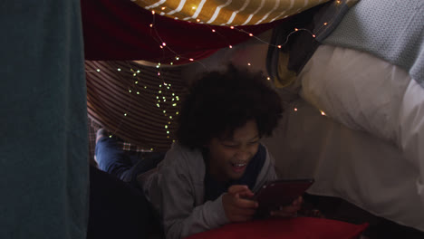 Mixed-race-girl-lying-in-bedroom-fort-using-digital-tablet