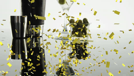 Golden-confetti-falling-over-bartender-equipment-and-olives-in-cocktail-glass-on-grey-background