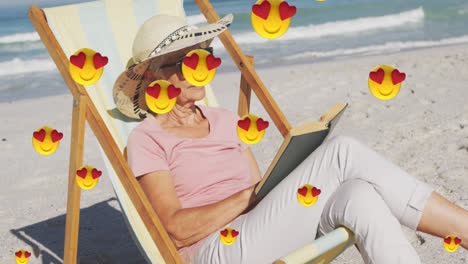 Animation-of-red-heart-love-emojis-digital-icons-over-woman-reading-book-in-deckchair-on-beach